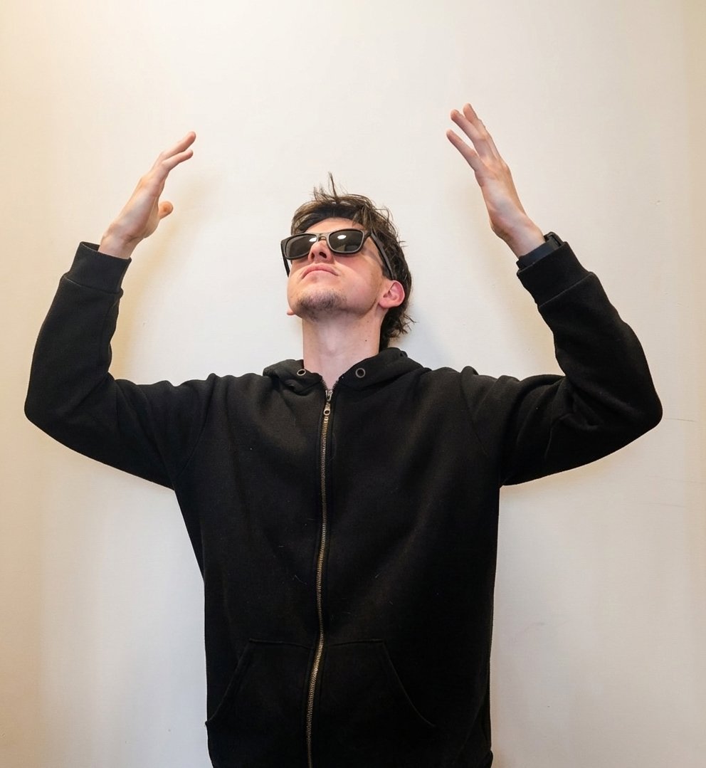 Tomas against a pale wall in a black hoodie and sunglasses, both arms raised as if the ceiling had just opened.